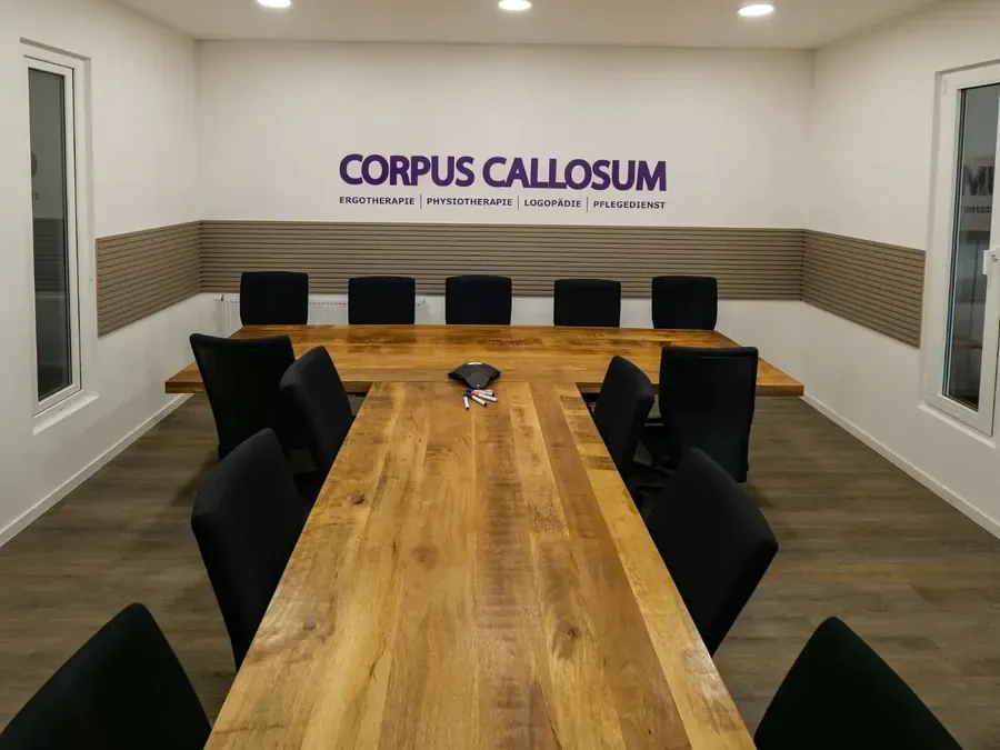 Besprechungsraum der Corpus Callosum GmbH mit langem Holztisch und Logowand